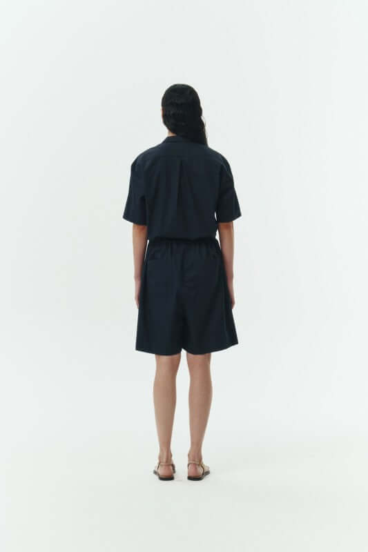 Back view of a model wearing the Emma Solid Jumpsuit in navy, showcasing its relaxed fit and camp collar design.