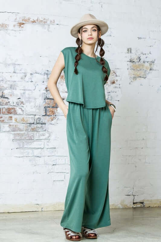 Open Front Wide Leg Jumpsuit in green with relaxed wide-leg design and twist-front detail, styled with a hat.
