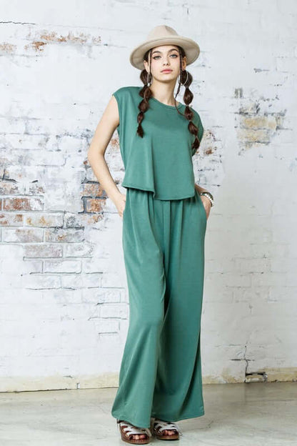 Open Front Wide Leg Jumpsuit in green with relaxed wide-leg design and twist-front detail, styled with a hat.
