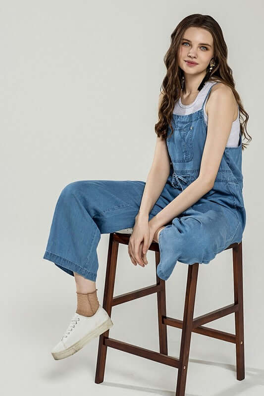 Plus Pocket Adjustable Straps Overall Jumpsuit worn by a model sitting on a wooden stool, showcasing casual chic style.