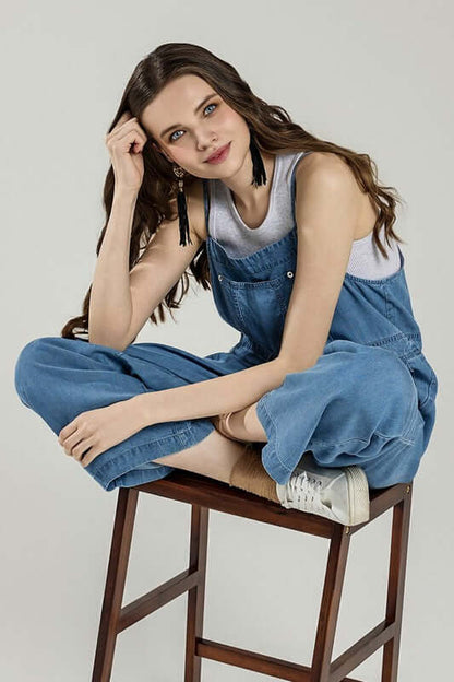 Model wearing a Plus Pocket Adjustable Straps Overall Jumpsuit, sitting on stool and showcasing casual chic style.