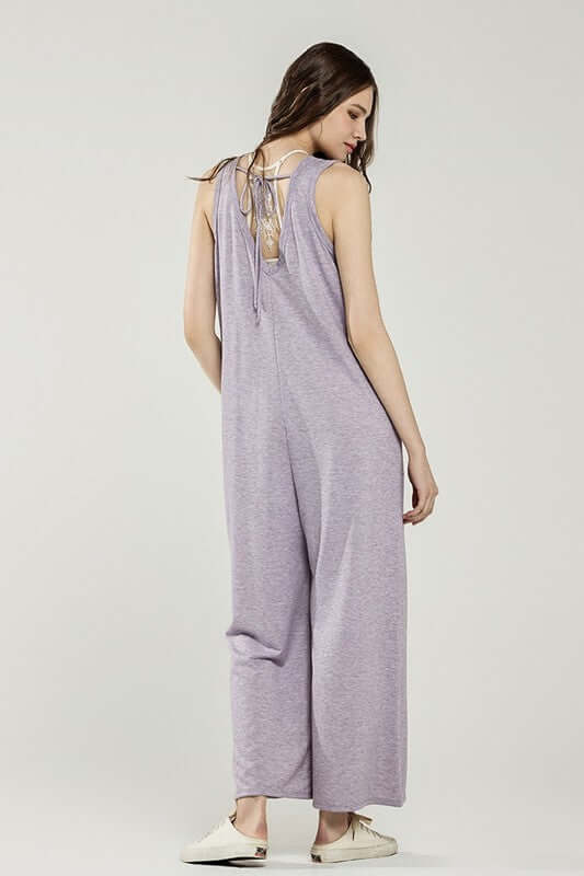 Back view of a woman wearing an Oversized Patched Pocket V-Neck Jumpsuit in lavender with drawstring detail.