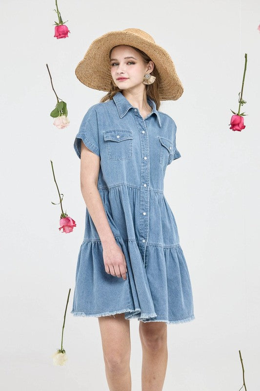 Model wearing a Button Down Tiered Babydoll Denim Shirt Dress with a straw hat, surrounded by hanging flowers.