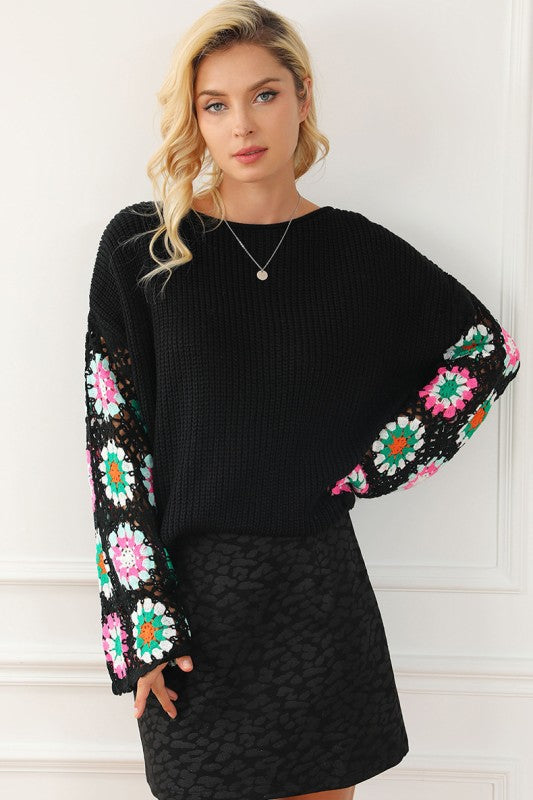 Woman wearing black floral crochet bell sleeve loose sweater with floral crochet sleeves and a ribbed design, styled with a skirt.