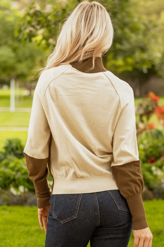 Back view of woman wearing Colorblock Raglan Puff Sleeve Mock Neck Sweater in beige and brown outdoors.